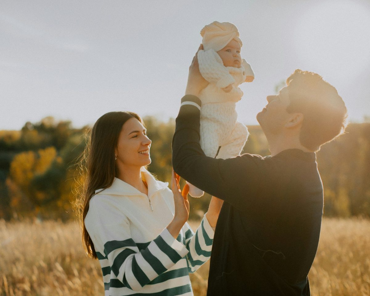 Smiling parents lifting their baby in a sunlit autumn field